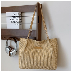 Detail of straw tote bag with brown leather strap, gold chain, and Fashion label