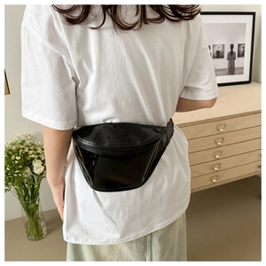 Close-up of a semi-circular black patent leather waist bag with reflective mirror finish
