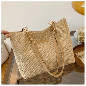 Detailed close-up of woven straw tote bag featuring leather logo and chain shoulder strap