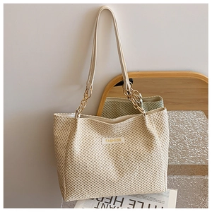 Detail of woven straw tote bag with gold chain strap and FASHION logo leather patch
