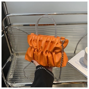 Détail du sac plissé orange avec poignée ornée de strass et fine chaîne en métal
