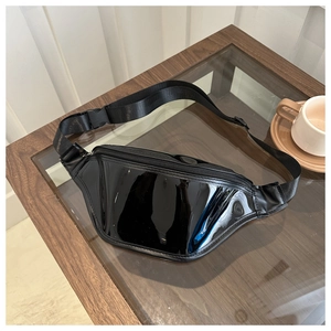 Detail view of black glossy patent leather chest bag with adjustable strap on a glass table