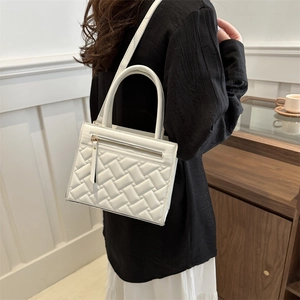 Fashionable white woven crossbody bag with top handles shown in minimalist interior setting