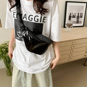 Fashionable black patent leather chest bag with adjustable strap worn by model in home setting