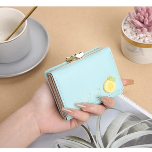 Primer plano de cartera corta plegable de PU azul claro con dije de piña y cierre de beso.