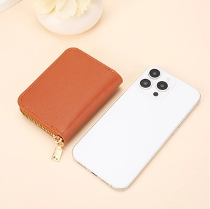 Brown litchi grain leather card holder with gold zipper next to a smartphone