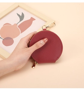 Petit porte-monnaie rond en cuir bordeaux avec fermeture éclair dorée en main