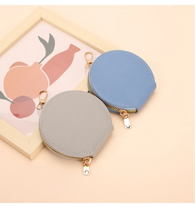 Détail de porte-monnaie ronds en cuir à texture litchi avec zips dorés et mousquetons