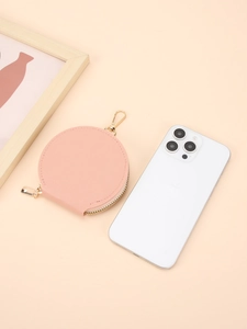Porte-monnaie rond en cuir rose avec fermeture éclair dorée et crochet sur fond neutre