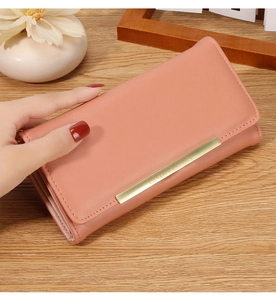 Detail of coral pink long leather wallet with gold metal bar on wooden tabletop