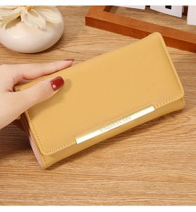 Detail view of mustard yellow long wallet showing golden metal logo and fine stitching detail