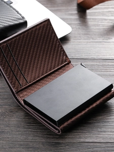 Brown leather pop-up wallet with carbon fiber texture and RFID protection on wooden desk