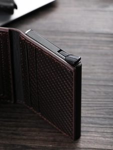 Men's RFID pop-up card holder in dark brown leather and carbon fiber on wood desk