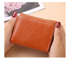 Nahaufnahme einer braun-orangen Ledergeldbörse mit goldenem Reißverschluss in den Händen