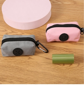 Close-up of gray and pink pet waste bag dispensers with metal carabiner on wooden surface