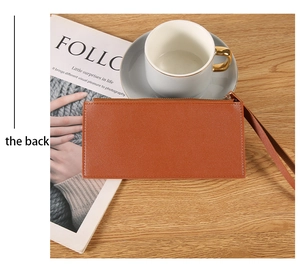 Slim long leather wallet in caramel brown with wristlet strap on a desk