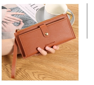 Detail of a brown lychee pattern leather long wallet with wristlet on a wooden table