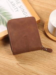 Vintage brown men's bifold wallet with zipper on a wooden table with coffee cup