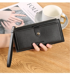 Detail of black long leather wallet with gold buckle and wristlet strap on wooden table