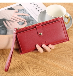 Close-up of red lychee leather wallet with gold hardware and a wrist strap on a desk