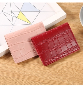Detail of red and pink croc-embossed card holders on a modern light wood tabletop