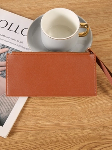 Brown faux leather long wallet with wristlet and zipper on a wooden surface