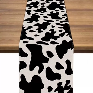 Rectangular table runner with black and white cow print on a rustic wooden table surface