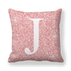 Détail d'une housse de coussin rose pailleté avec une lettre J majuscule blanche au centre