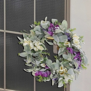 Close-up of artificial wreath featuring purple orchids and grey flocked leaves on a glass door