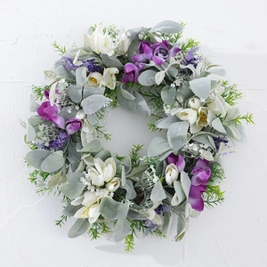 Artificial spring wreath with purple flowers and silver leaves on a white wall