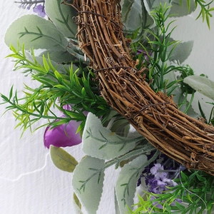 Detail of purple silk flowers and flocked greenery on a dry rattan wreath base