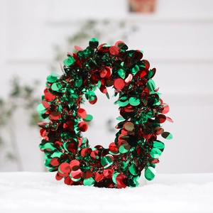 Detail of red and green sequined festive wreath standing on white faux snow backdrop