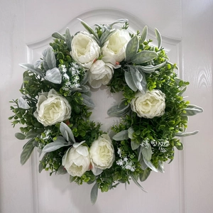 Detail of white peony and eucalyptus wreath on a white wooden door with rustic leaves