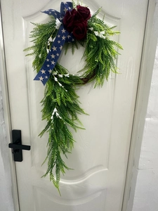 Close-up of decorative artificial wreath with green ferns and red roses on a white door