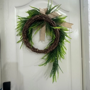 Detail of rustic door wreath with green fern leaves and burlap bow on white wood