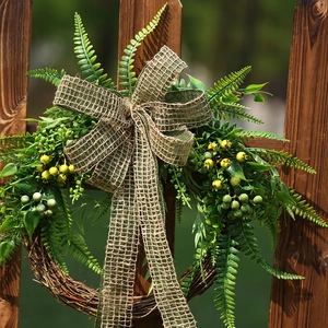 Artificial greenery wreath with yellow berries and a burlap bow on a wooden fence