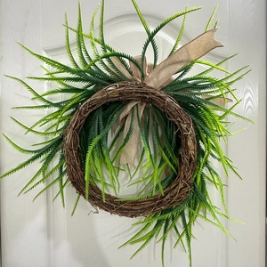 Detail of farmhouse wreath featuring faux willow leaves, rattan base, and burlap bow