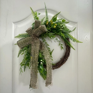 Detail of faux green plant wreath with burlap bow on white door for garden decoration