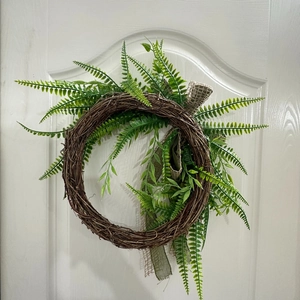Detailed view of rustic branch wreath with green fern leaves and a burlap ribbon