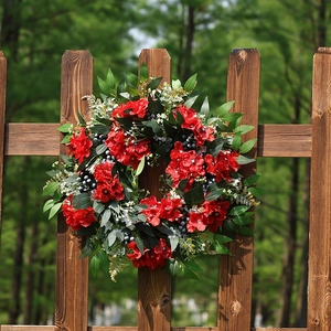 Couronne de fleurs artificielles rouges et feuilles vertes sur une clôture en bois
