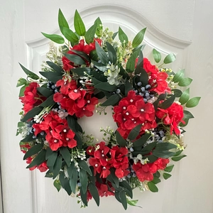 Détail d'une couronne de fleurs rouges artificielles et baies bleues sur porte blanche
