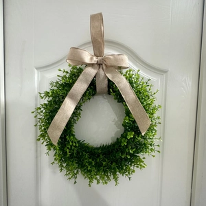 Close-up of a green eucalyptus wreath with a burlap bow hanging on a white wooden door