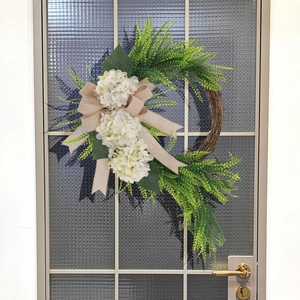 Detail of white hydrangea wreath with green fern leaves and a burlap bow on glass door
