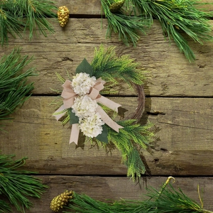 Detail of farmhouse wreath with white hydrangeas, green ferns, and a burlap bow on wood