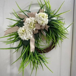 Detail of white hydrangea wreath with burlap bow and fern leaves on white wooden door