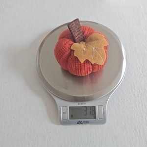 Macro view of a knitted pumpkin ornament on a scale showing its 31.8g weight and texture
