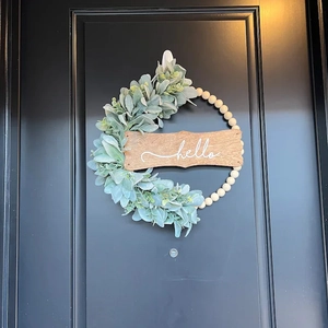 Detail of wooden bead wreath with sage leaves and white hello script sign on black door