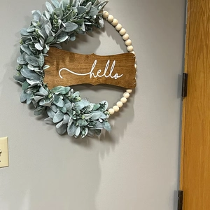 Detail of wooden bead wreath with frosted leaves and a dark Hello sign for wall decor