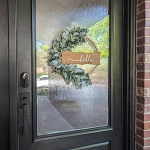 Detail of wooden bead wreath with green leaves and a hello sign hanging on a glass door