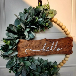 Detail of hello wooden sign with realistic green leaves and rustic beads on a white door